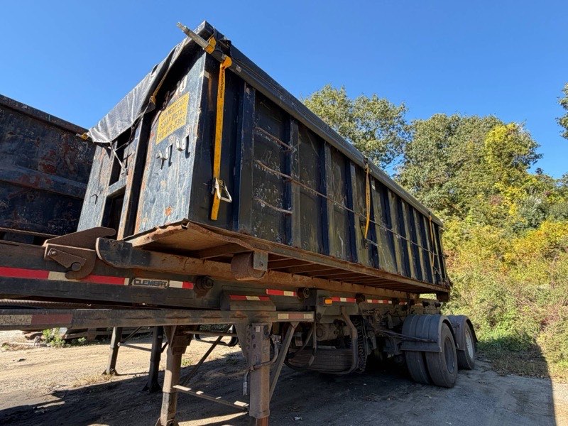 A tarped roll-off container loaded on a trailer in the yard